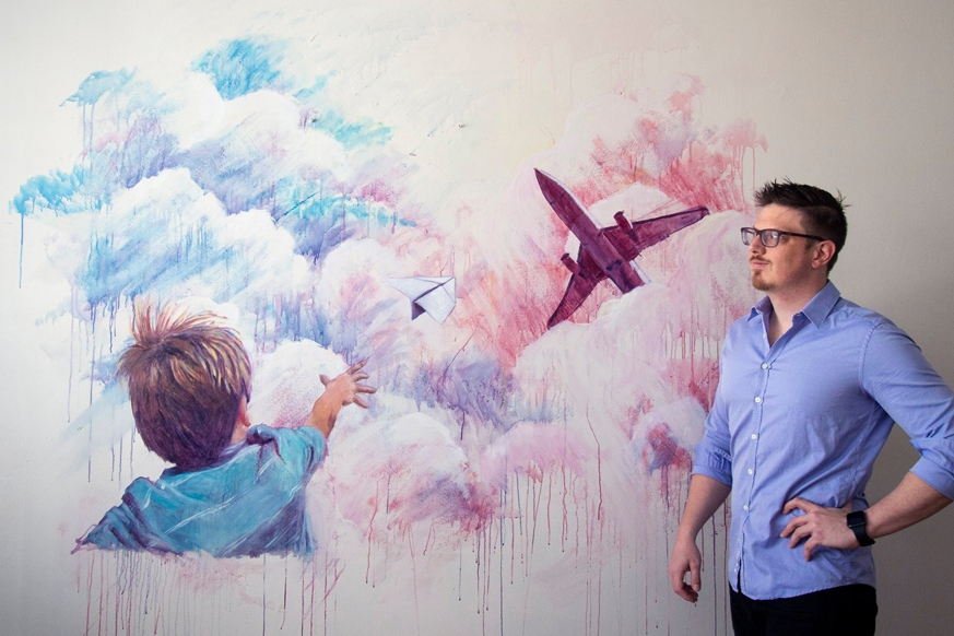 Luc standing in front of a mural he painted